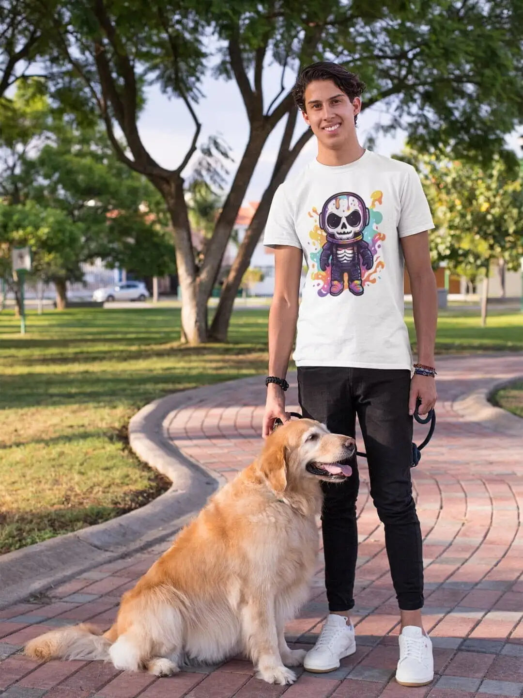 A young man wearing a white t-shirt with a colorful skeleton graphic and black pants, standing with a golden retriever dog