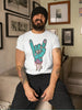 A bearded man wearing a black beanie and a white t-shirt with a cartoon zombie hand making the 